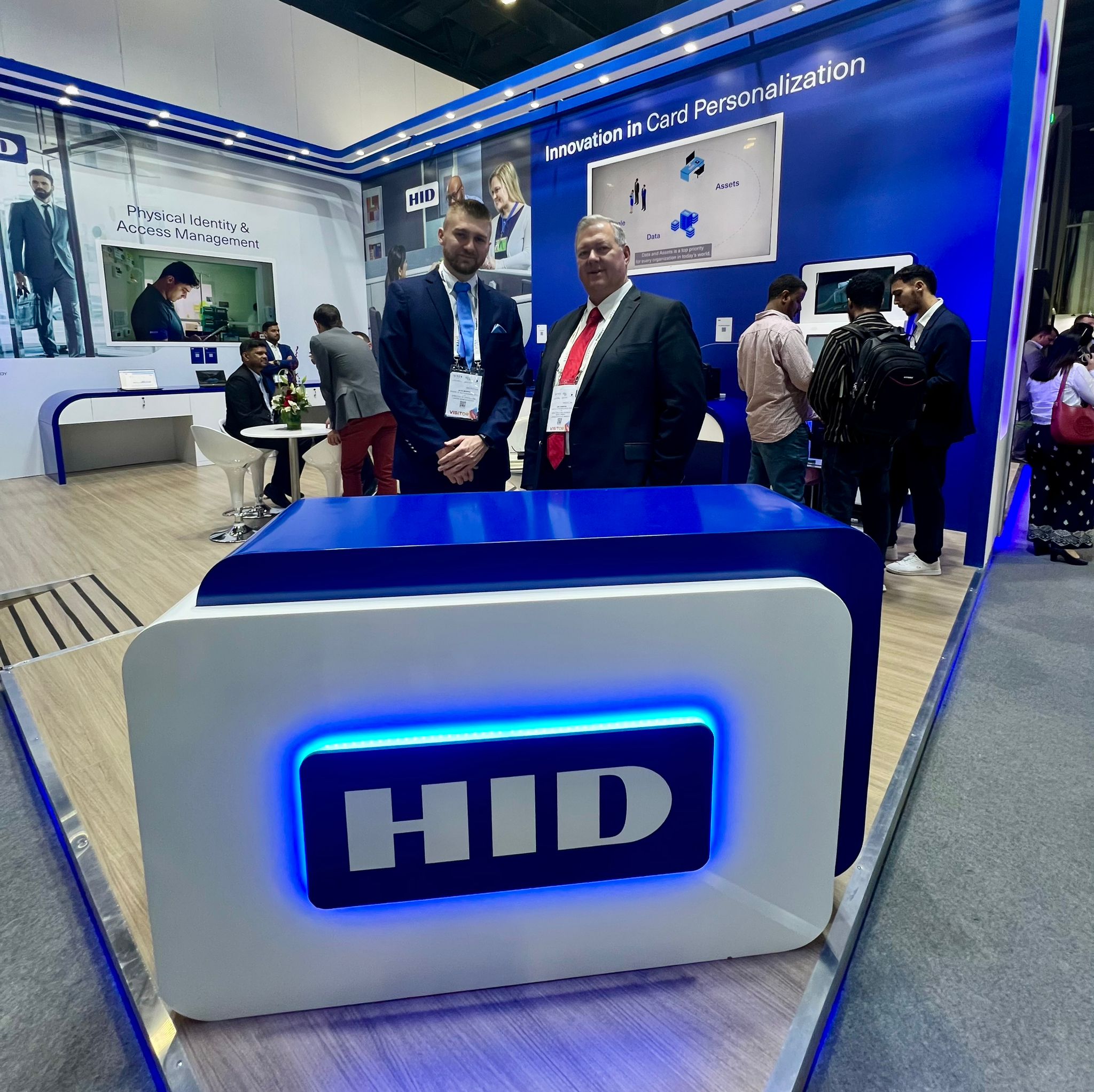 Jean Murphy, Director of Digital ID Technologies, standing with Andrew Munik in front of a display stand featuring the HID logo, showcasing their range of FARGO card printers.